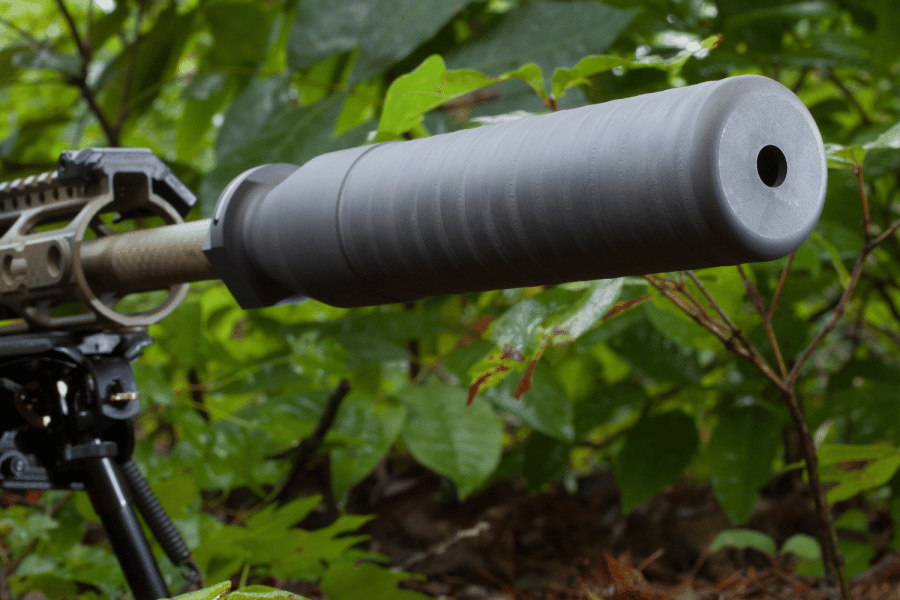 2A Marketplace: Private Firearm Classifieds A close-up view of a rifle with a large silencer attached to the barrel, set outdoors among green foliage—a scene echoing recent suppressor deregulation state bills gaining traction across the country. Private sale of guns.