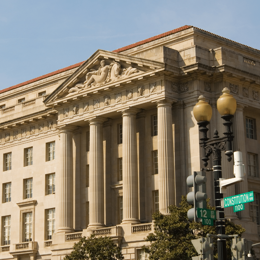 2A Marketplace: Private Firearm Classifieds Neoclassical government building with columns and a sculpted pediment, partially visible streetlights, and a street sign reading Constitution Ave in the foreground—an iconic scene reminiscent of recent attention as the site of the AR-15 ban Supreme Court case. Private sale of guns.