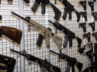 2A Marketplace: Private Firearm Classifieds Several rifles and firearms are displayed on a metal grid wall rack, with various styles and colors arranged in rows, showcasing their different stocks, barrels, and grips. Private sale of guns.