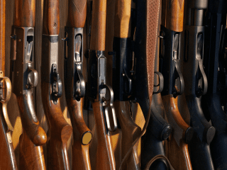 2A Marketplace: Private Firearm Classifieds A row of rifles with wooden and synthetic stocks is arranged upright in a gun rack, showing the triggers and receivers. Private sale of guns.