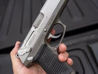 2A Marketplace: Private Firearm Classifieds A hand holding a silver and black Ruger semi-automatic handgun, with focus on the details and branding on the grip and slide, against a dark textured background. Private sale of guns.
