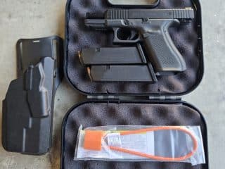 2A Marketplace: Private Firearm Classifieds A black handgun in a foam-lined case with two magazines, a holster, a cable lock, a cleaning rod, and a gun brush on a concrete surface. Private sale of guns.